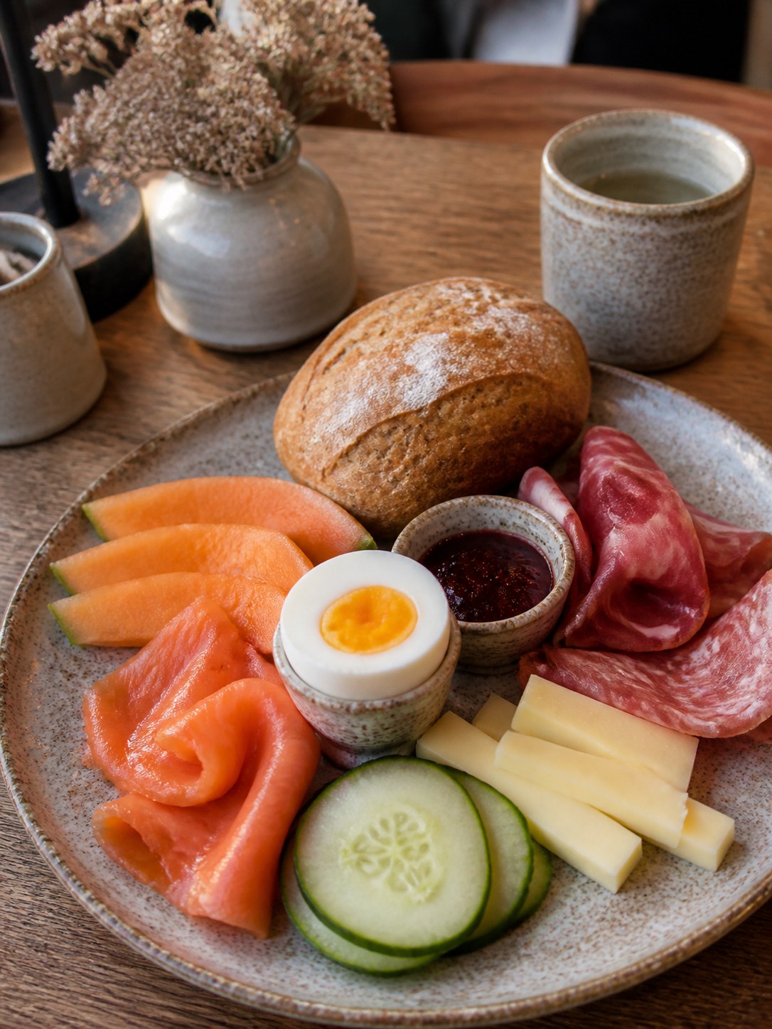Frühstücksteller mit Lachs, Schinken, Salami, Käse, gekochtem Ei, Gurke, Melone, Marmelade und einem Rundstück.