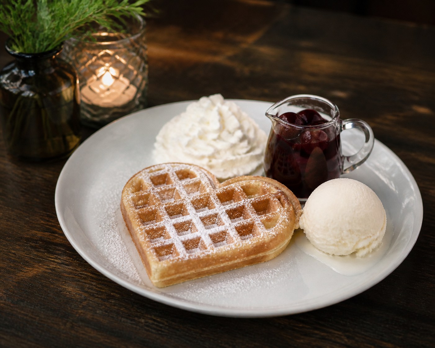 Waffel mit Puderzucker, einer Kugel Vanilleeis, Sahne und einem Glas heißer Kirschen.